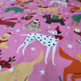 Pink fabric with a festive Christmas print featuring dalmatian dogs, reindeer, Santa Claus, snowman, Christmas trees, and white stars.