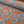 A close-up of patterned fabric with a bright orange background and blue toile-style tropical and scenic print, with one rolled section showing the material drape.
THE DRESSMAKER FABRICS