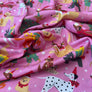 Pink fabric with a festive Christmas animal print featuring a Dalmatian, a cat in a sweater, a reindeer, a dog, and other holiday motifs.