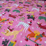 Pink Christmas-themed fabric featuring a playful pattern of various dogs dressed in holiday attire, including Santa, reindeer, and snowman outfits, with stars and gift boxes.
